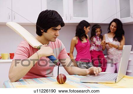 Young man holding a cricket bat and using a laptop in the kitchen View Large Photo Image Stock Image - Young man holding a cricket bat and using a laptop in the kitchen. Fotosearch