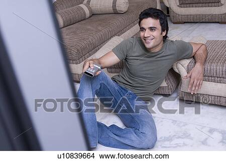Picture - Young man holding a remote control and smiling. Fotosearch