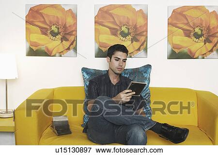 Stock Photo - Young man sitting on the couch and holding a CD case. Fotosearch