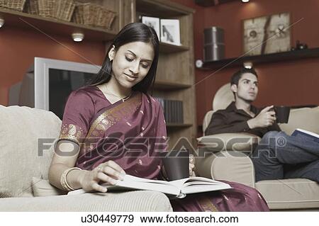 Stock Photo - Young woman reading a book with a young man holding a mug. Fotosearch