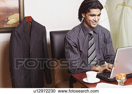 Businessman sitting in an office and using a laptop View Large Photo Image Stock Image - Businessman sitting in an office and using a laptop. Fotosearch