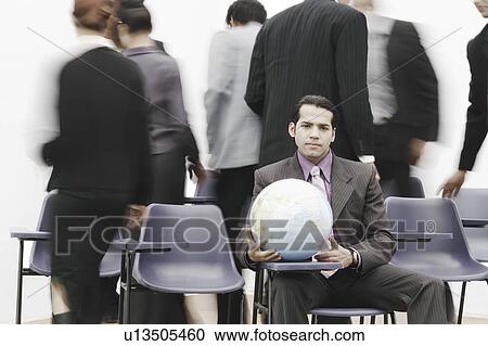 Stock Image - Portrait of a businessman sitting in a meeting holding a globe. Fotosearch