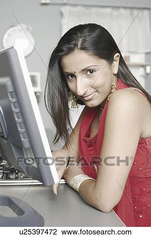 Stock Image - Portrait of a young woman sitting in front of a computer monitor. Fotosearch