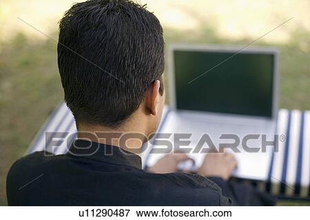Stock Photo - Rear view of a mid adult man using a laptop. Fotosearch