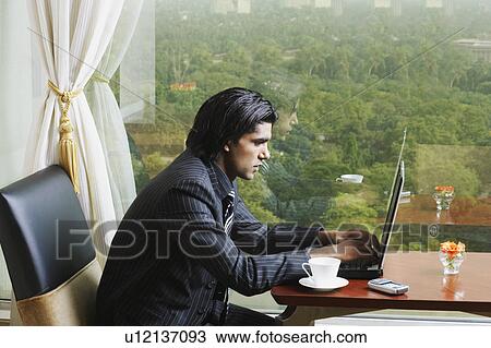 Side profile of a businessman sitting in an office and using a laptop View Large Photo Image Stock Image - Side profile of a businessman sitting in an office and using a laptop. Fotosearch