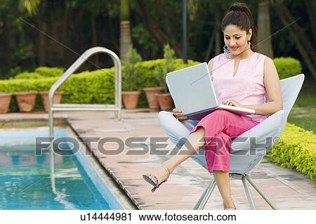 Young woman using a laptop at the poolside View Large Photo Image Stock Image - Young woman using a laptop at the poolside. Fotosearch