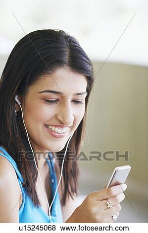 Stock Photo - Close-up of a young woman wearing headphones and holding an MP3 player. Fotosearch