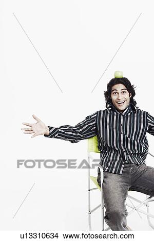 Portrait of a young man with his arms outstretched balancing an apple on his head View Large Photo Image Picture - Portrait of a young man with his arms outstretched balancing an apple on his head. Fotosearch