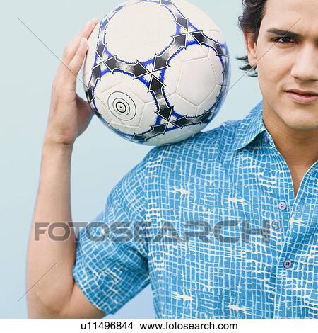 Picture - Close-up of a young man holding a soccer ball on his shoulder. Fotosearch