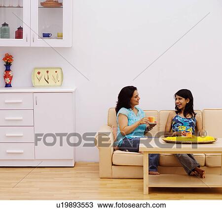 Stock Image - Mid adult woman with a young woman sitting on a couch and talking to each other. Fotosearch