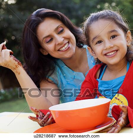 Stock Photo - Mid adult woman with her daughter sitting at a table and smiling. Fotosearch