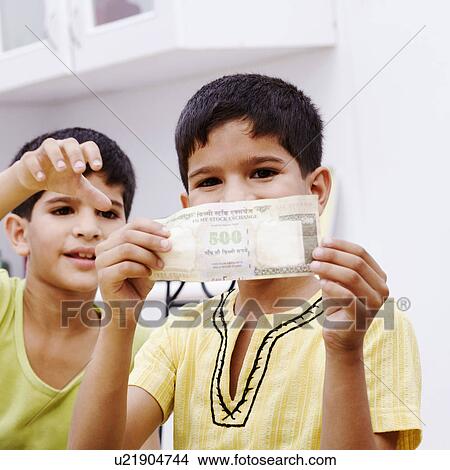 Picture - Portrait of a boy holding an Indian five hundred rupee note with his brother taking it. Fotosearch