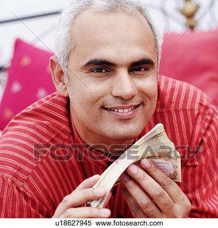 Stock Photography - Portrait of a mid adult man holding Indian currency notes and smiling. Fotosearch