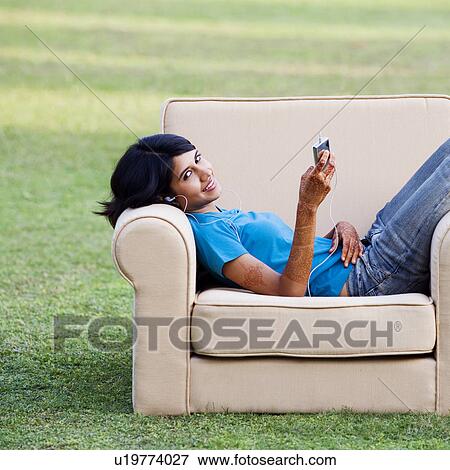 Stock Photo - Portrait of a young woman lying in an armchair and listening to an MP3 player. Fotosearch