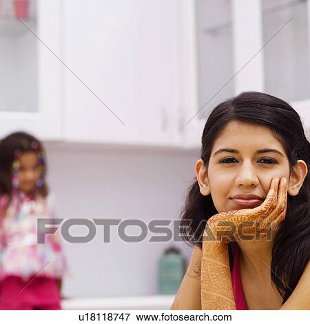 Portrait of a young woman with her hand on her chin with a girl sitting in the background View Large Photo Image Stock Photo - Portrait of a young woman with her hand on her chin with a girl sitting in the background. Fotosearch