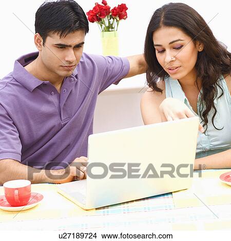 Young couple sitting in front of a laptop View Large Photo Image Picture - Young couple sitting in front of a laptop. Fotosearch