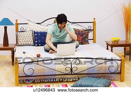 Stock Image - Young man using a laptop on the bed. Fotosearch