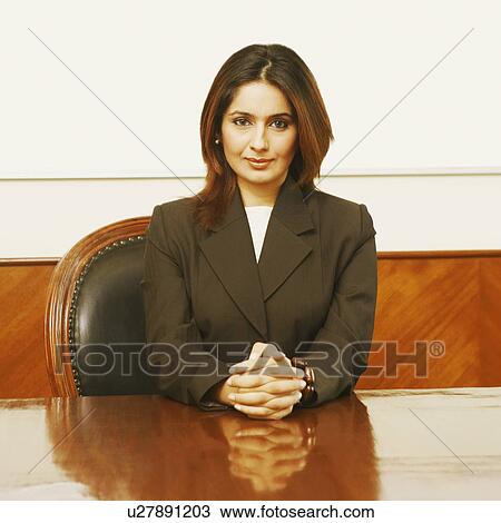 Stock Image - Portrait of a businesswoman sitting in a conference room with her hands clasped. Fotosearch