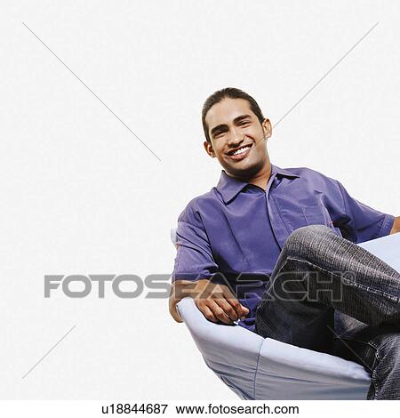 Portrait of a young man sitting on a chair with his legs crossed at the knee View Large Photo Image Stock Photo - Portrait of a young man sitting on a chair with his legs crossed at the knee. Fotosearch