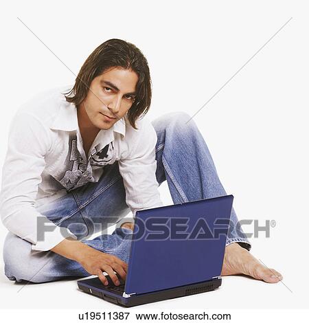 Stock Photo - Portrait of a young man sitting on the floor and using a laptop. Fotosearch