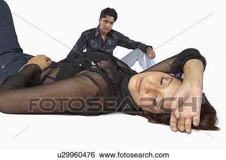 Stock Photograph - Close-up of a young woman lying on the floor with a young man sitting beside her. Fotosearch