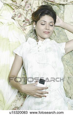 Stock Image - High angle view of a young woman listening to an MP3 player. Fotosearch