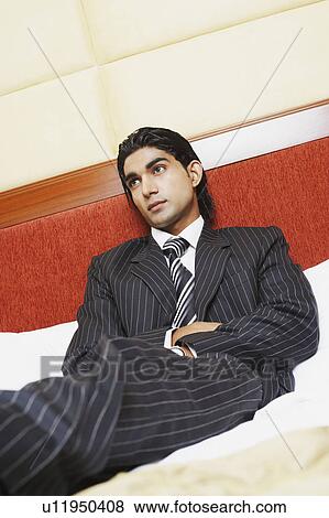 Low angle view of a businessman reclining on the bed View Large Photo Image Stock Photo - Low angle view of a businessman reclining on the bed. Fotosearch