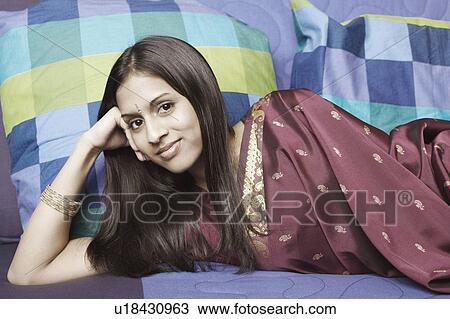 Stock Image - Portrait of a young woman lying on a couch with her hand on her head. Fotosearch