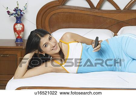 Portrait of a young woman lying on the bed and holding a mobile phone View Large Photo Image Stock Image - Portrait of a young woman lying on the bed and holding a mobile phone. Fotosearch