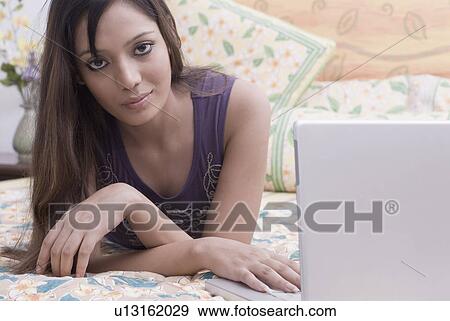 Portrait of a young woman lying on the bed and using a laptop View Large Photo Image Stock Photo - Portrait of a young woman lying on the bed and using a laptop. Fotosearch