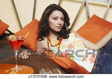 Stock Photograph - Portrait of a young woman reclining on a couch with a martini glass on the table. Fotosearch