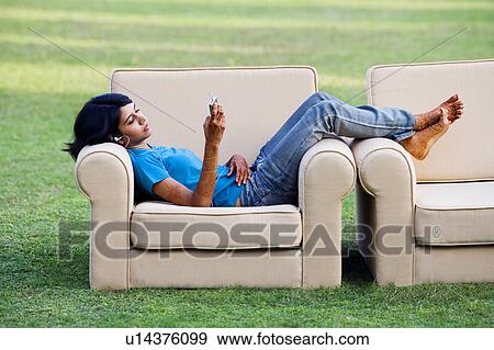Stock Photo - Side profile of a young woman lying in an armchair and listening to an MP3 player. Fotosearch