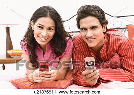 Young couple lying on the bed and holding mobile phones View Large Photo Image Stock Image - Young couple lying on the bed and holding mobile phones. Fotosearch