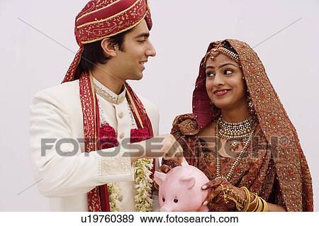 Bride holding a piggy bank with a groom putting money in it View Large Photo Image Stock Photo - Bride holding a piggy bank with a groom putting money in it. Fotosearch