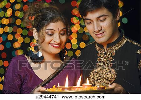 Stock Image - Close-up of a young couple holding a plate of religious offerings and smiling. Fotosearch