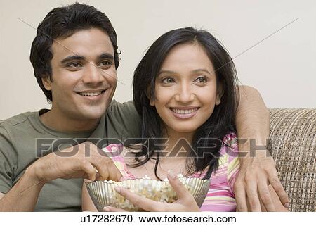 Stock Image - Close-up of a young couple smiling and eating popcorn. Fotosearch