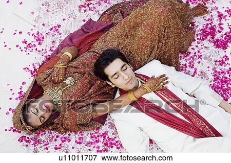 Stock Photo - High angle view of a newlywed couple in traditional wedding outfits sleeping on the bed. Fotosearch
