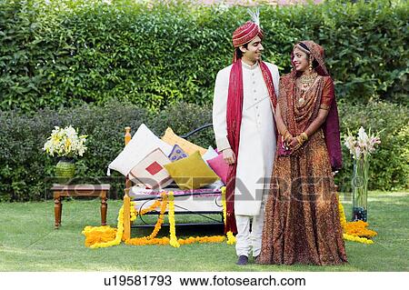 Newlywed couple in traditional wedding dress standing in front of a bed in a lawn View Large Photo Image Stock Image - Newlywed couple in traditional wedding dress standing in front of a bed in a lawn. Fotosearch