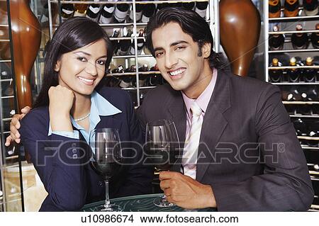 Picture - Portrait of a businesswoman and a businessman sitting with glasses of red wine in a wine cellar. Fotosearch