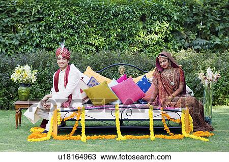 Portrait of a newlywed couple in traditional wedding dress sitting on the bed in a lawn View Large Photo Image Stock Image - Portrait of a newlywed couple in traditional wedding dress sitting on the bed in a lawn. Fotosearch