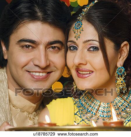 Stock Photo - Portrait of a young couple holding a plate of religious offerings and smiling. Fotosearch