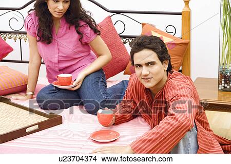 Picture - Young couple holding cups of tea in the bedroom. Fotosearch