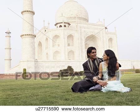 Stock Image - Young couple sitting in front of a mausoleum, Taj Mahal, Agra, Uttar Pradesh, India. Fotosearch