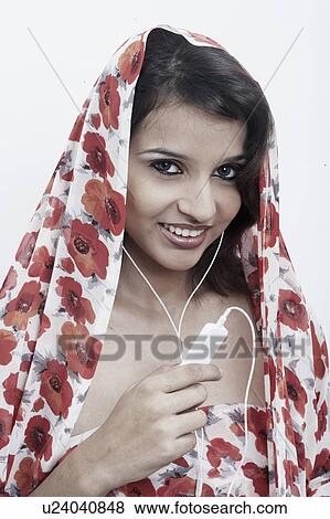 Stock Photo - Portrait of a young woman with a stole on her head listening to an MP3 player. Fotosearch