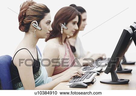 Stock Image - Side profile of three businesswomen working on computers in an office. Fotosearch