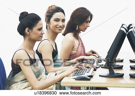 Stock Image - Side profile of three businesswomen working on computers in an office. Fotosearch