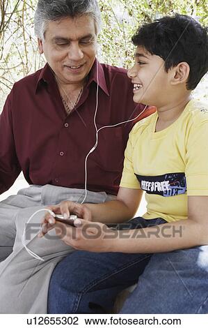 Stock Image - Close-up of a mature man and his grandson looking at an MP3 player. Fotosearch