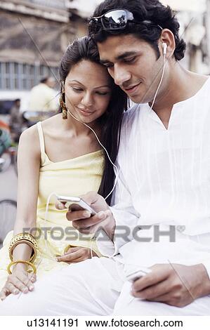 Stock Image - Close-up of a young couple sitting on a rickshaw and listening to an MP3 player. Fotosearch