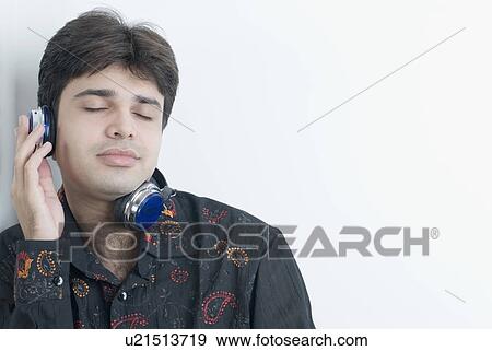 Close-up of a young man listening to music with his eyes closed View Large Photo Image Stock Photo - Close-up of a young man listening to music with his eyes closed. Fotosearch