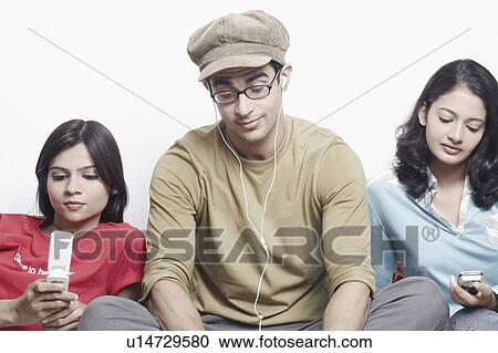 Stock Image - Close-up of a young man sitting between two young women. Fotosearch
